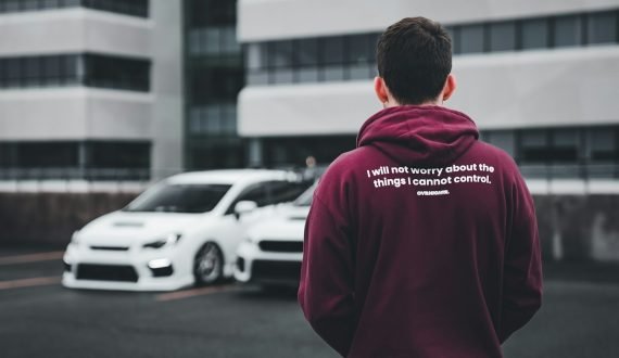 a man in a maroon hoodie standing in front of a white car